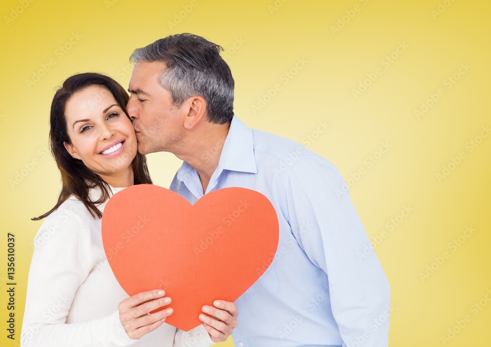 Mature man kissing a woman holding red heart