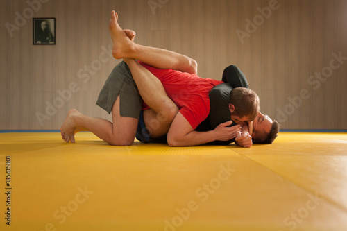 MMA fighter holding his opponent with triangle hold and trying to choke his neck