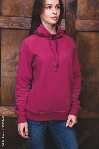 Young woman wearing blank magenta sweatshirt with area for your logo or design, mock-up of template magenta sweatshirt, wooden wall in the background photo