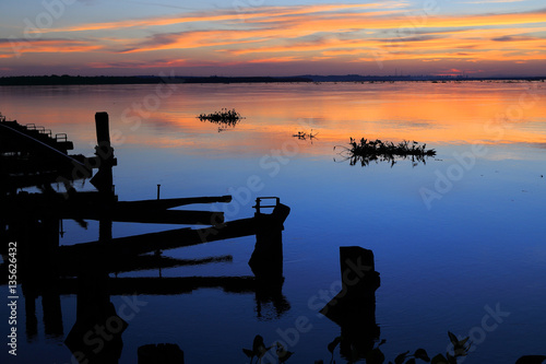 Beautiful sunset on the river parana in entre rios, Argentina, south america. An old wooden pier, the sky in orange tones is reflected on the water and aquatic plants pass by the river. photo