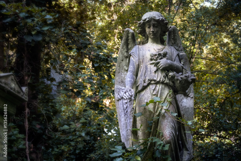 Young angel statue with flowers in a London cemetery looks down Young angel statue with flowers in a London cemetery looks down