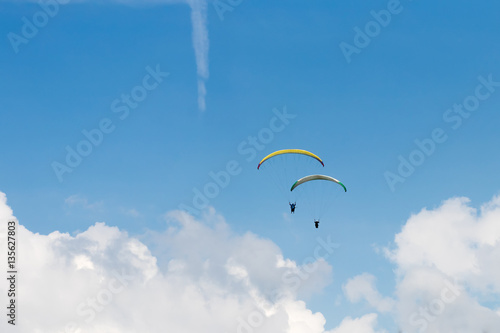 Two people parasailing under blue sky over white clouds
