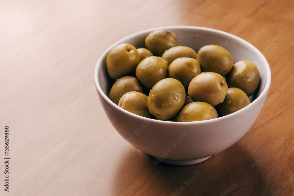 Fresh green olives in white bowl on wooden table background. Fresh green olives in white bowl on wooden table background.