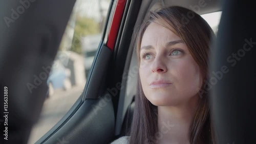 Beautiful woman looking outside through the window in the backseat of a car. She looks worried and sad. Close up.
