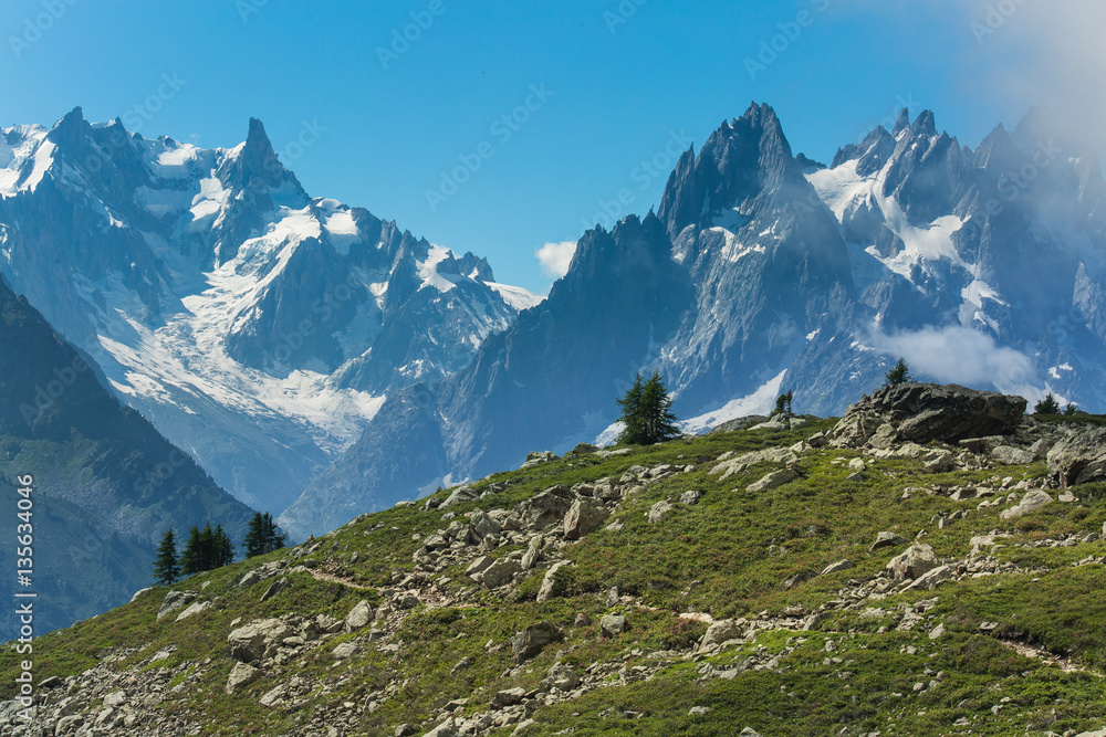 Boulder field and grassy meadows in the French Alps above Chamonix. Hiking trail crosses the foreground hill.