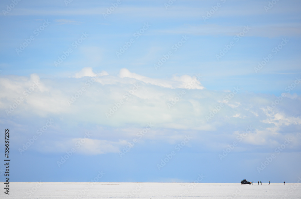 Fototapeta premium Céu azul com núvens no salar de Uyuni com pessoas e carro à distância