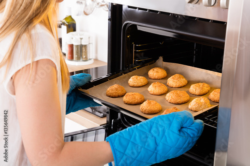 Woman Placing Tray Full Of Cookies In Oven
