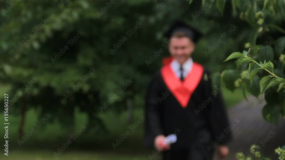 Male student in academic dress walking and jumping with joy in park, graduation Male student in academic dress walking and jumping with joy in park, graduation
