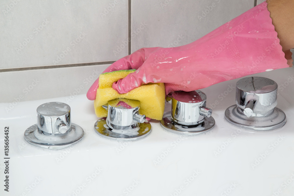 In the bathroom, hand in protective glove washing and polishing bath jacuzzi water taps. Maid or housewife cleans house. General cleaning or regular wash up. In the bathroom, hand in protective glove washing and polishing bath jacuzzi water taps. Maid or housewife cleans house. General cleaning or regular wash up.