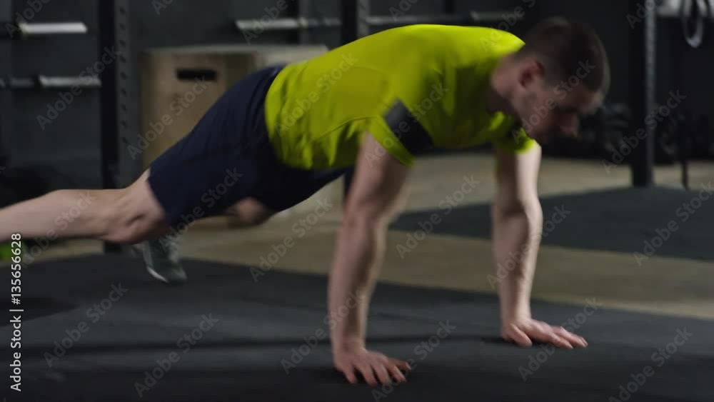 Tracking with side view of strong sportsman performing burpee or squat thrust exercise during cross-training workout Tracking with side view of strong sportsman performing burpee or squat thrust exercise during cross-training workout