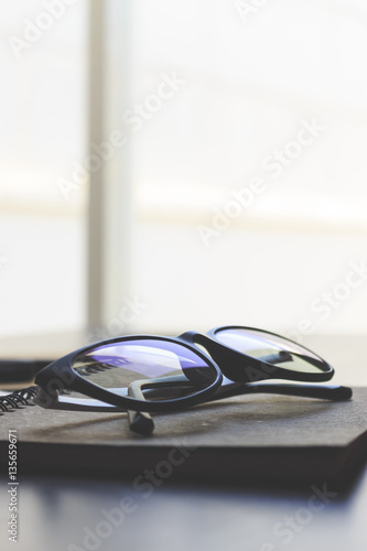 glasses and book on wooden table. film colors tone and soft-focus in the background. over light 