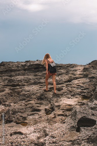 Blonde hair girl with a backpack walking along the cliff
