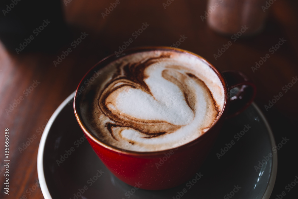 A red cup of coffee with white foam on the wooden table A red cup of coffee with white foam on the wooden table