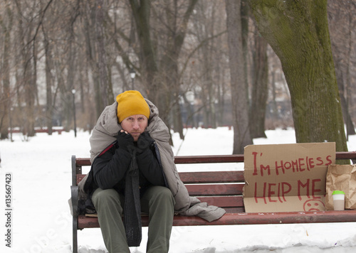 
Adult homeless man with cardboard  in  winter city park sit on bench
