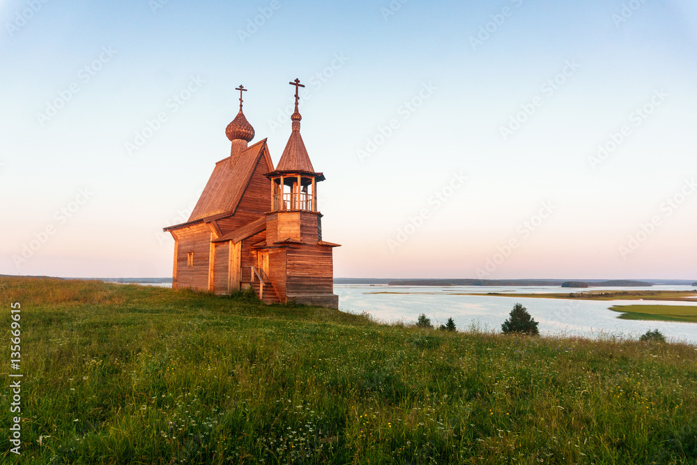 Wooden church on the top of the hill. Vershinino village sunset view. Arkhangelsk region, Northern Russia.