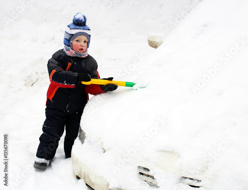 The little boy cleans a car from the snow