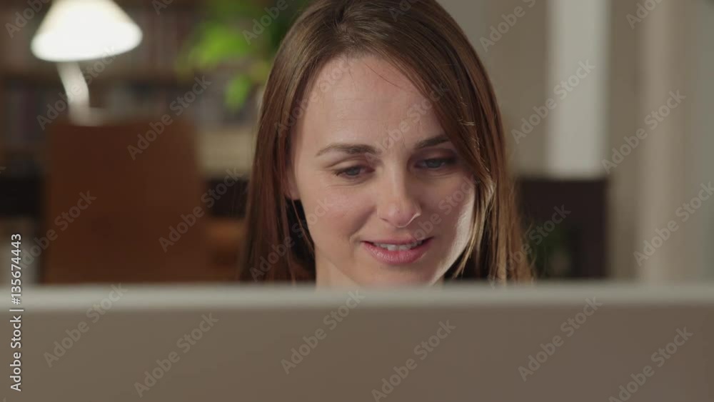Young woman watches videos on internet in her laptop at home. She smiles and watches very concentrated. Extreme close up with the laptop at foreground. Young woman watches videos on internet in her laptop at home. She smiles and watches very concentrated. Extreme close up with the laptop at foreground.