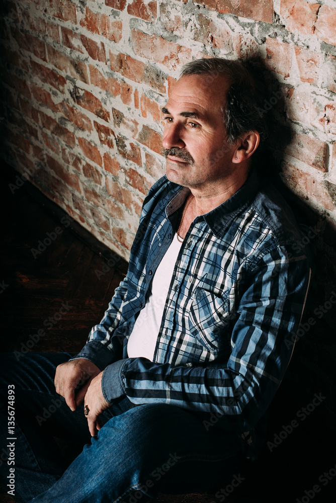 Handsome middle aged man is dressed in a casual clothing. Red brick wall background.