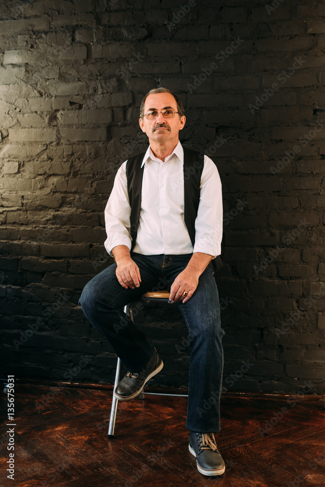 Handsome middle aged man is dressed in a white shirt and a black vest. Black background. Handsome middle aged man is dressed in a white shirt and a black vest. Black background.