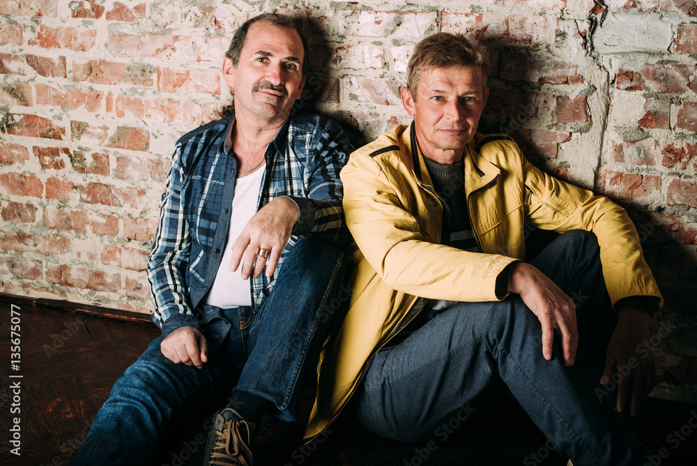 Two handsome middle aged men, dressed in casual clothing , old friends. Red brick wall background. Two handsome middle aged men, dressed in casual clothing , old friends. Red brick wall background.