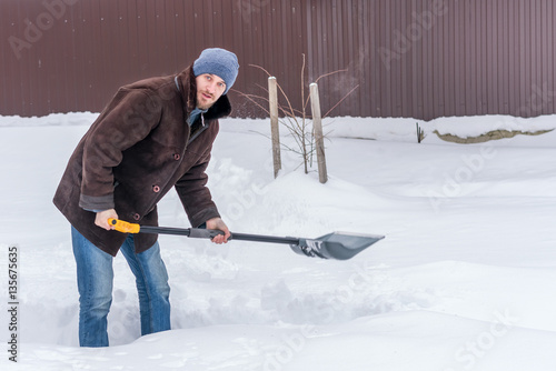 Man in winter clothes cleans snow shovel on courtyard