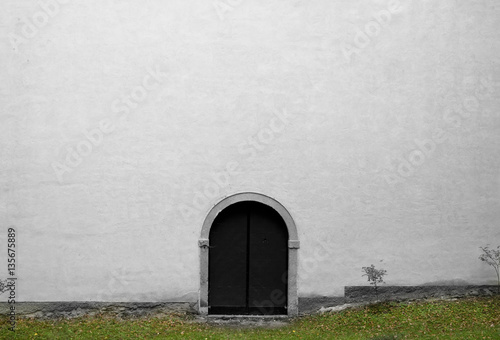 Big white wall with small wooden door. Architecture detail of old church