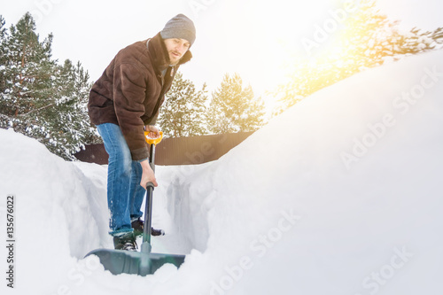 Fotografia Man in winter clothes cleans snow shovel on courtyard at sunny day