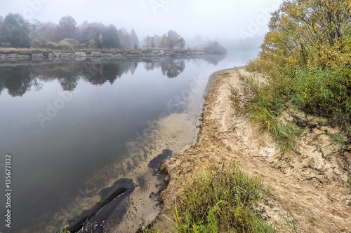 Coast of the autumn river in a fog.