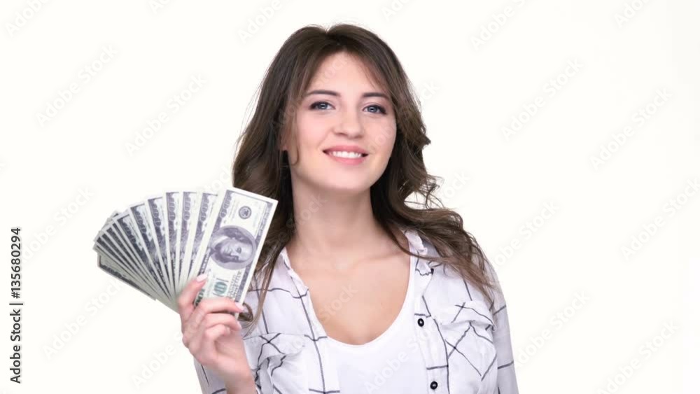 Happy young woman holding money in her hands and pointing finger away while standing isolated on white Happy young woman holding money in her hands and pointing finger away while standing isolated on white