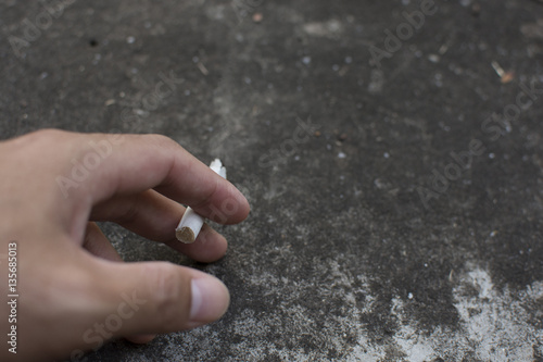 Man hand holding a cigarette with smoke on cement background.