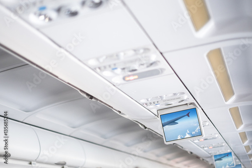 Control and information elements for passenger in white interior of modern aircraft, White interior space airliner, Display interior airliner, Advertising displays in aircraft interior