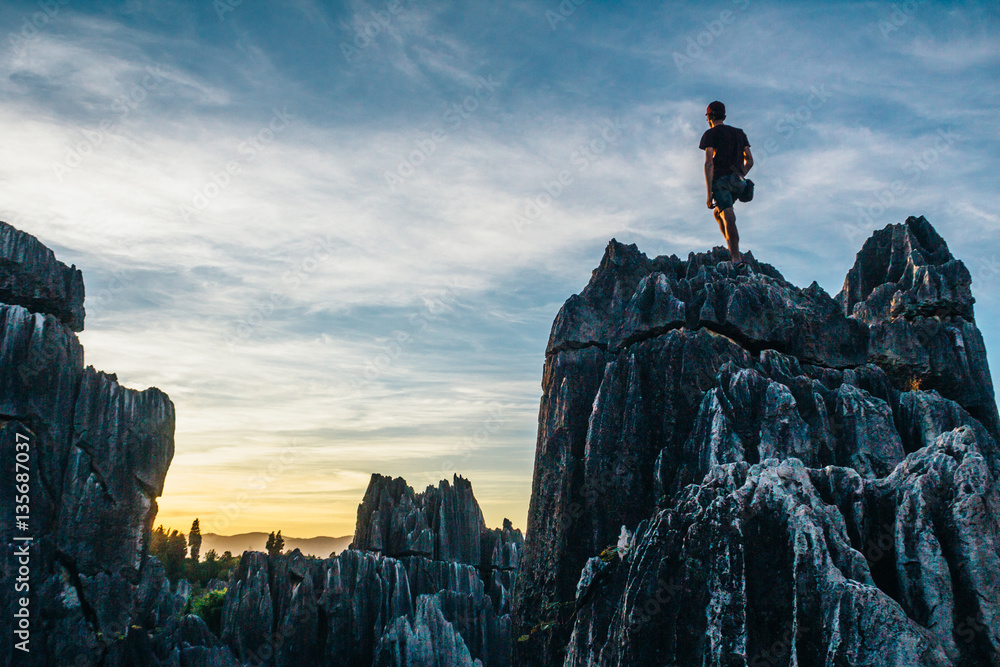 Boy admiring colorful sunset in Stone Forest in Shilin, Yunnan Province, South China, not far from the Kunming. It is world-famous natural area of limestone formations and UNESCO World Heritage Site.