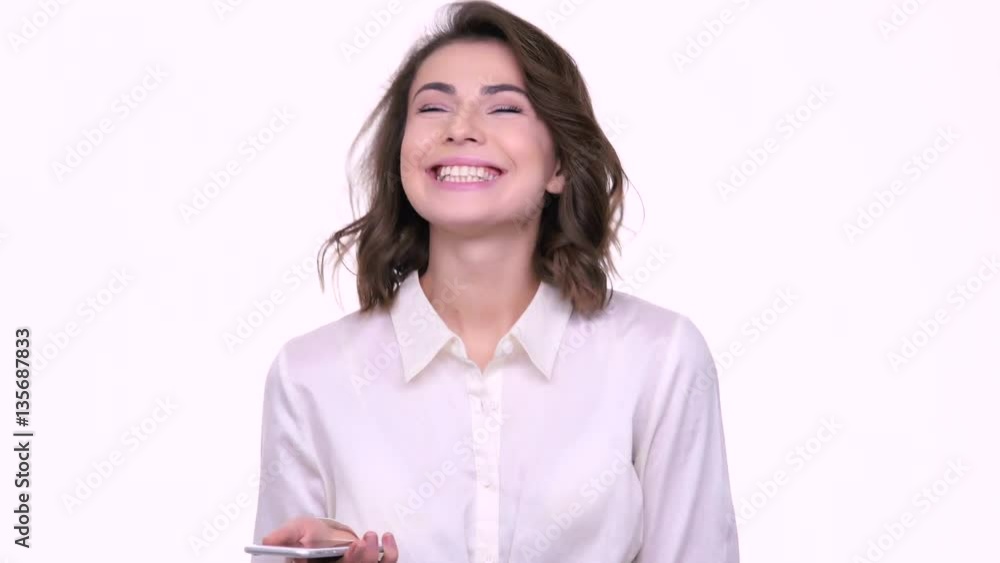 Cheerful teenage girl holding mobile phone and looking at it with smile while standing isolated on white Cheerful teenage girl holding mobile phone and looking at it with smile while standing isolated on white