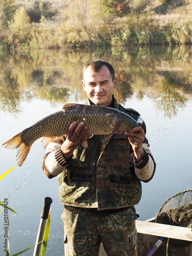 Fisherman With fish Mirror Carp. Fishing on river on autumn
