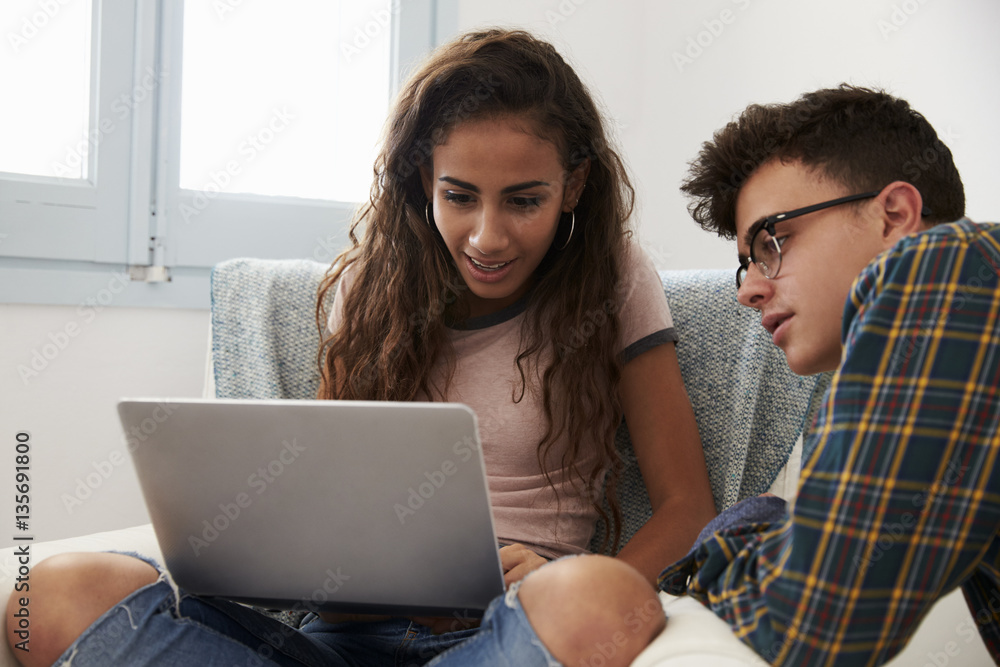 Teenage couple looking at laptop computer together at home