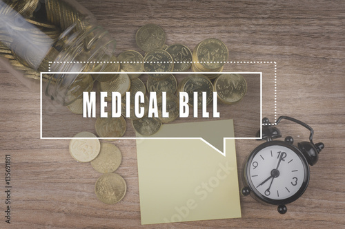 Coins spilling out of a glass jar on wooden background with MEDICAL BILL text . Financial Concept