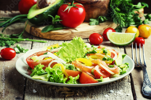 Salad with avocado, salmon, lettuce, onions and peppers on a pla