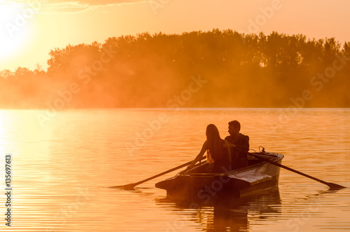 Love and romantic golden river sunset. Silhouette of couple on boat backlit by sunlight