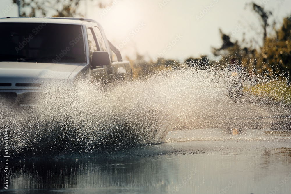 Obraz premium Motion car rain big puddle of water spray from the wheels through flood water after hard rain.Stop action ( capture with the high speed shutter) and selective focus,color toned.