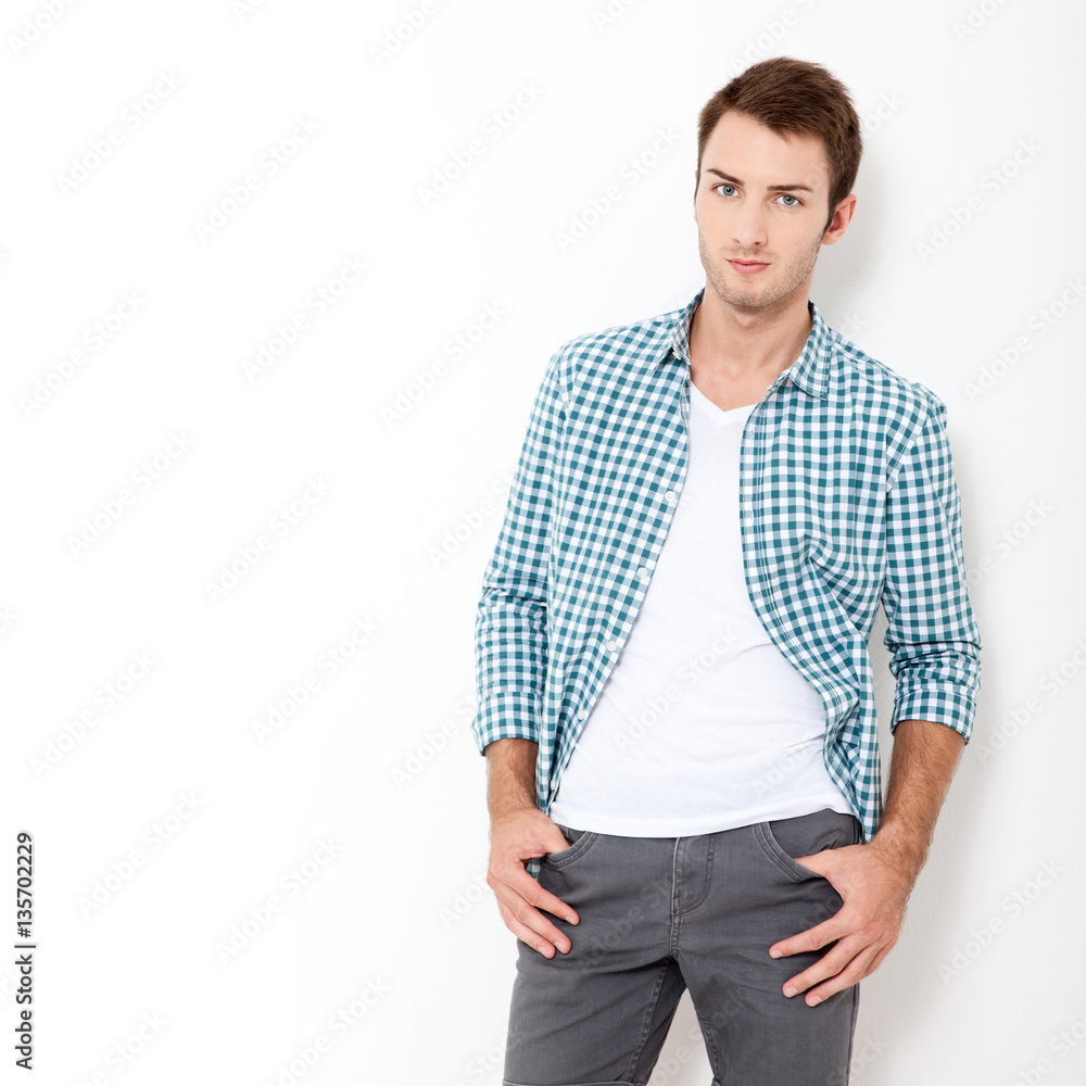 Fototapeta premium Happy young man. Portrait of handsome young man in casual shirt keeping arms crossed and smiling while standing against white background