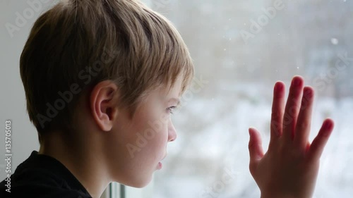 the child sits on the window-sill and looking out the window to the snow close-up