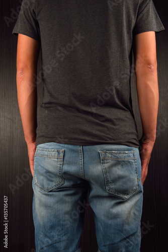 Back of young man wearing grey blank t-shirt, standing in a stud