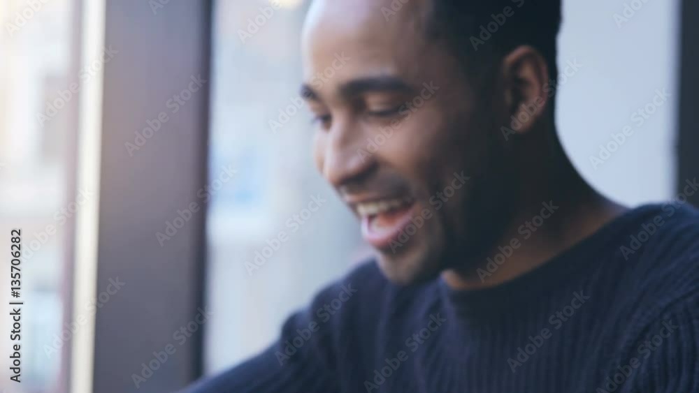 Cheerful afro american guy wearing smartwatch and playing on mobile phone in cafeteria Cheerful afro american guy wearing smartwatch and playing on mobile phone in cafeteria