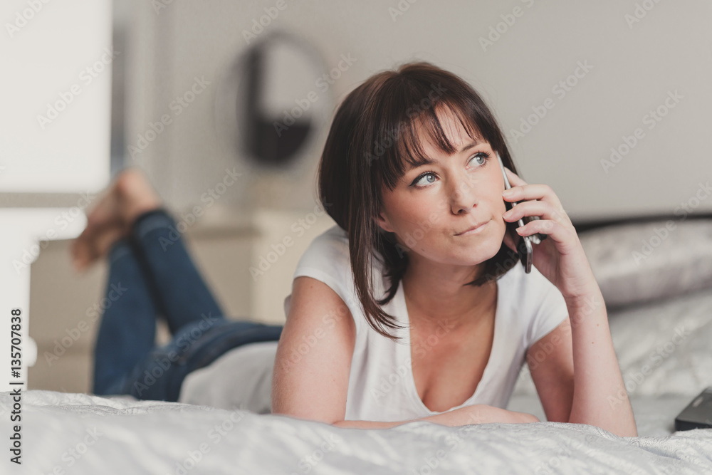beautiful woman talking on smartphone in her bedroom beautiful woman talking on smartphone in her bedroom