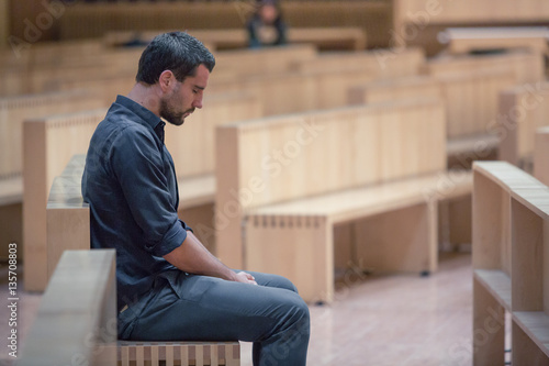 Young beard man wearing blue shirt praying in modern church