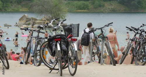 Bicycles on the Sandy Bank of Lake Bolko, People, Dressed in Sport Uniform and Swimsuits, Walking, Swimming, Playing, and Lying at the Bank of the Picturesque Lake photo