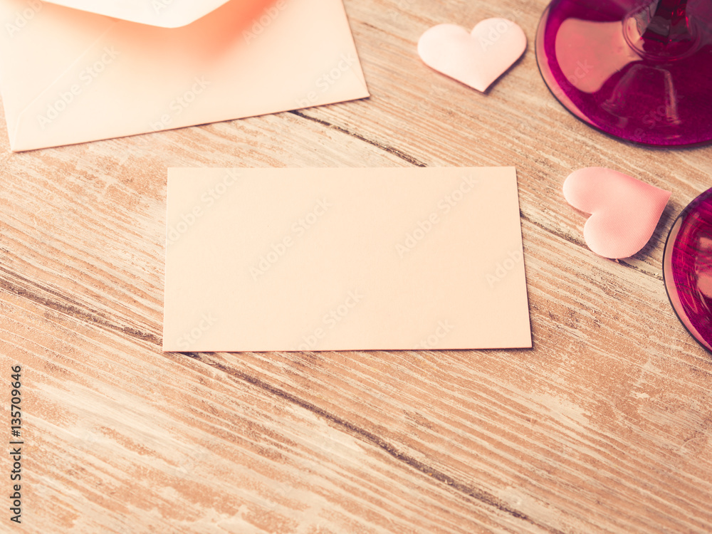 Fototapeta premium Blank pink paper letter note with hearts to fill with your text on wooden textured background. Valentine's day wedding romantic date invitation. Toned