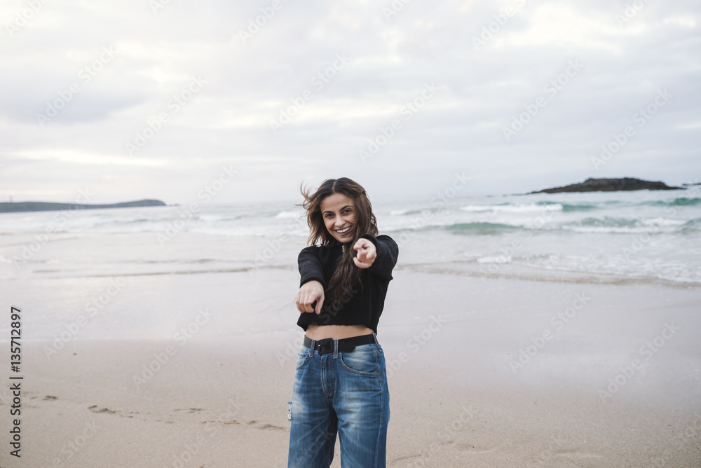 Portrait of happy young woman on the beach pointing on viewer