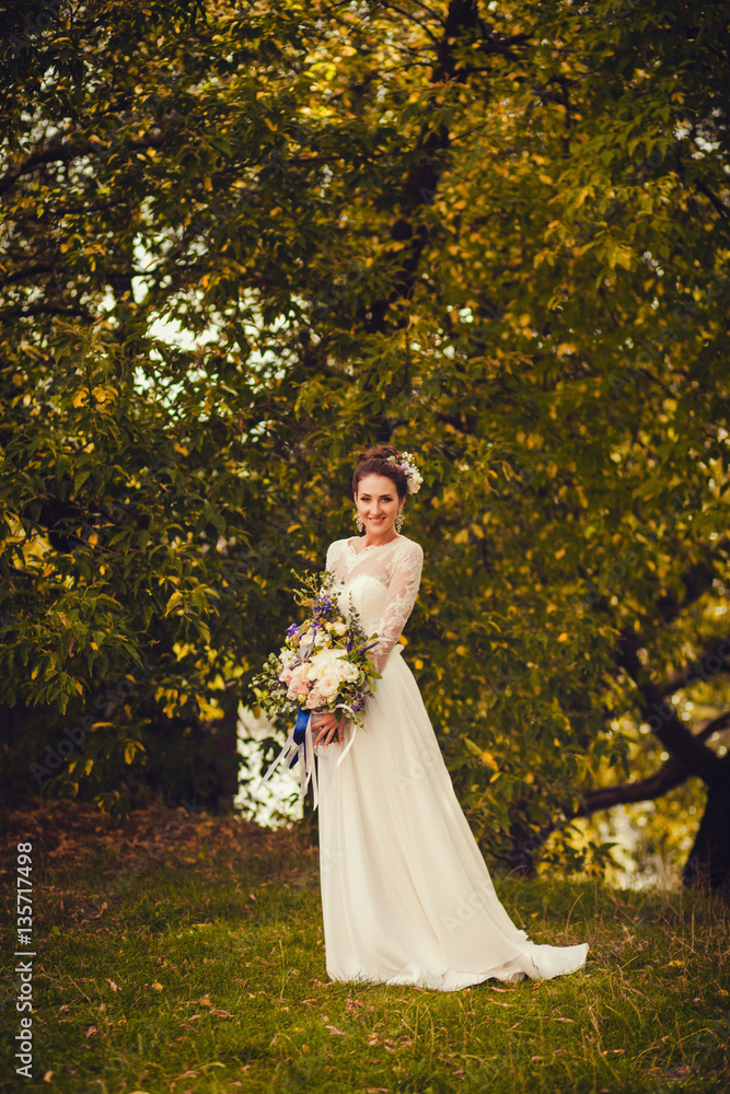 Beautiful stylish bride in a beautiful dress with flowers in the park