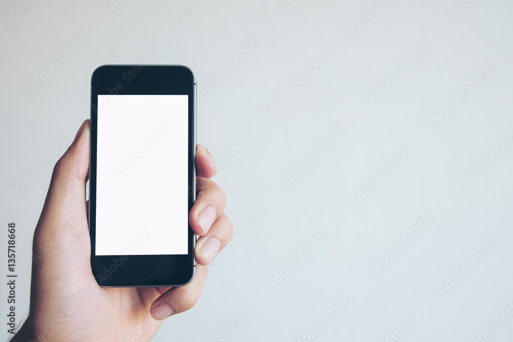 Mockup image of hand holding black mobile phone with blank white screen on white background room Mockup image of hand holding black mobile phone with blank white screen on white background room